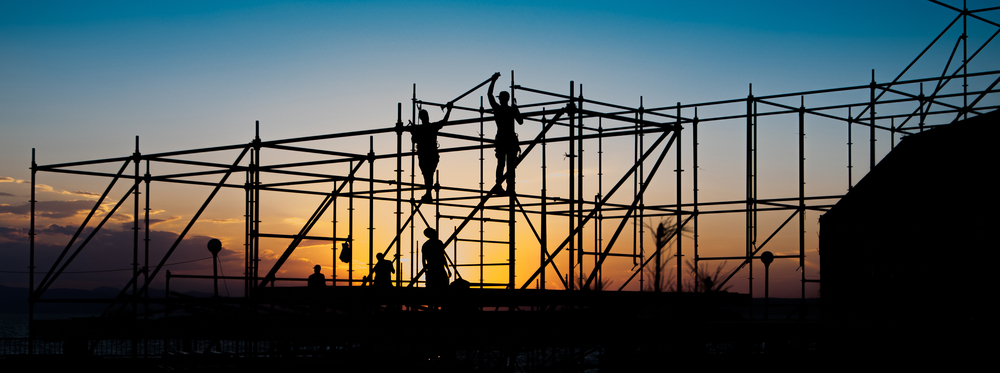 Silhouetted construction workers on scaffolding during sunset