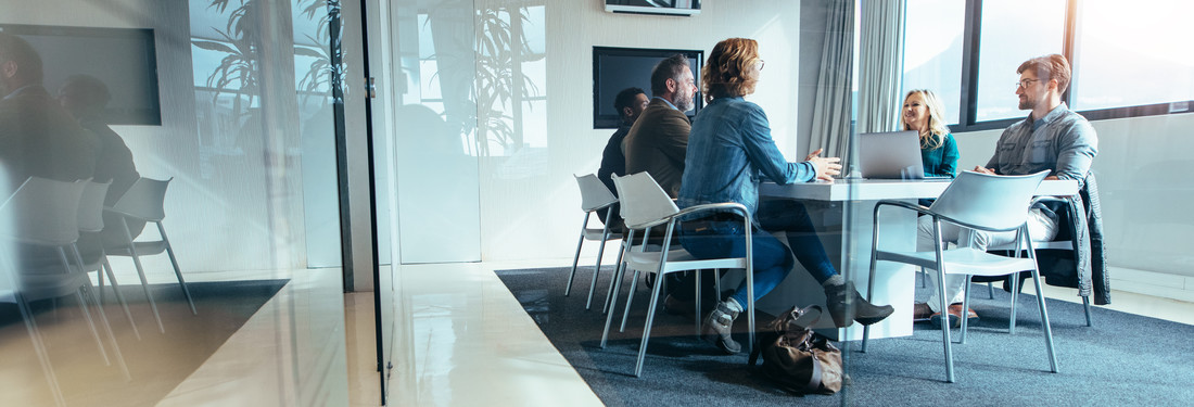 Office colleagues gathered around a table for a discussion in a workplace setting.